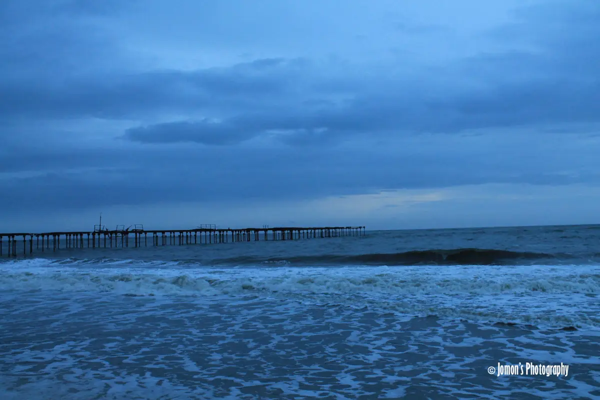 Distant pier at Alappuzha beach with deep blue sea and waves in evening light