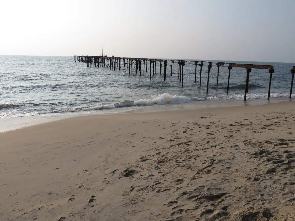 Old pier posts leading into the surf at Alappuzha beach with a sandy shore