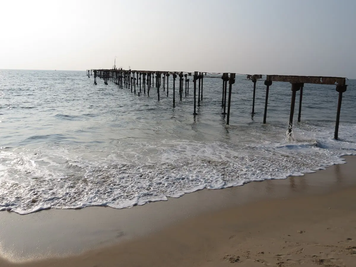 Pier posts and gentle surf on the beach at Alappuzha under a pale sky
