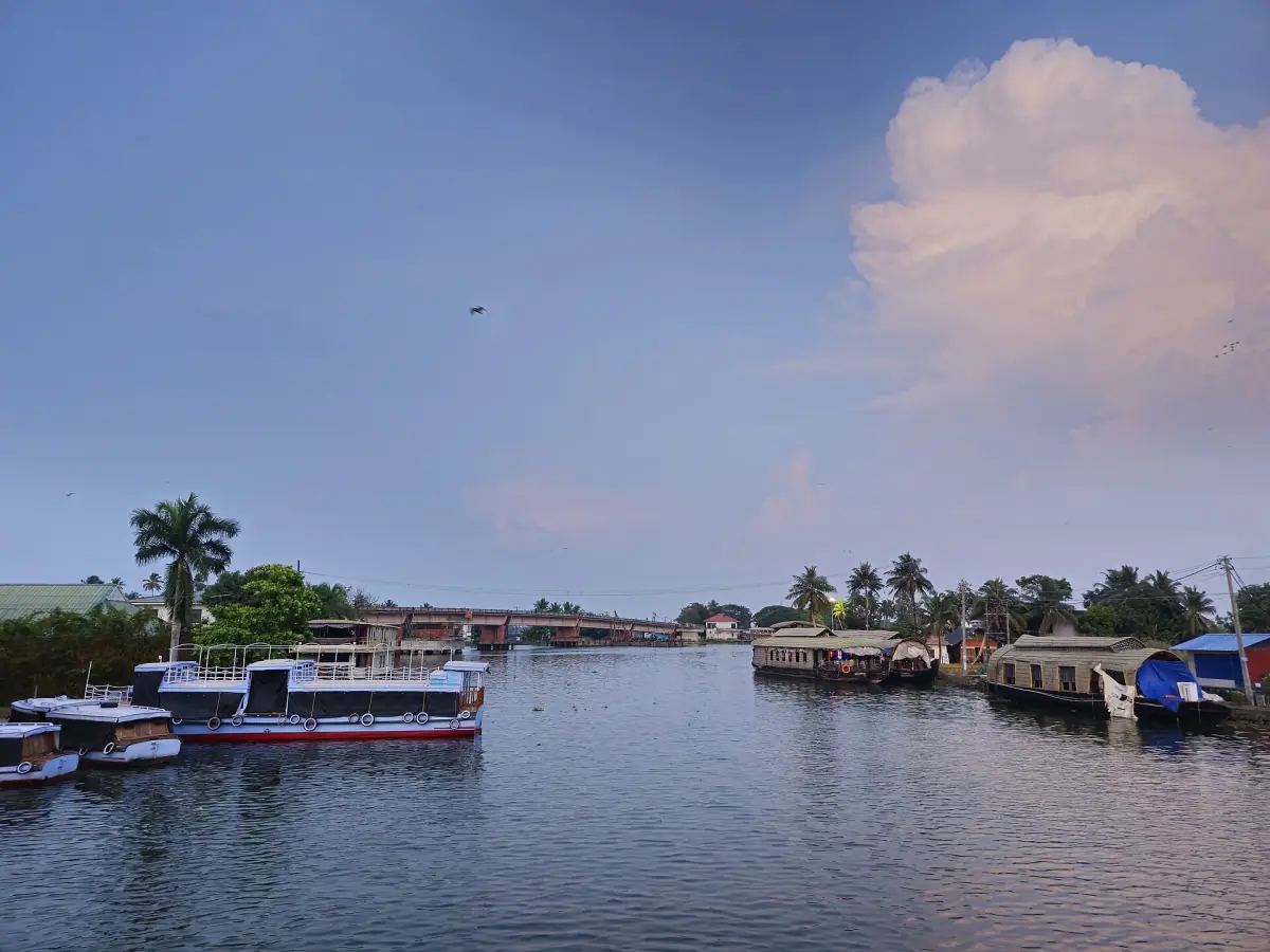 Boats and houseboats moored along a canal jetty in Alappuzha under a bright sky