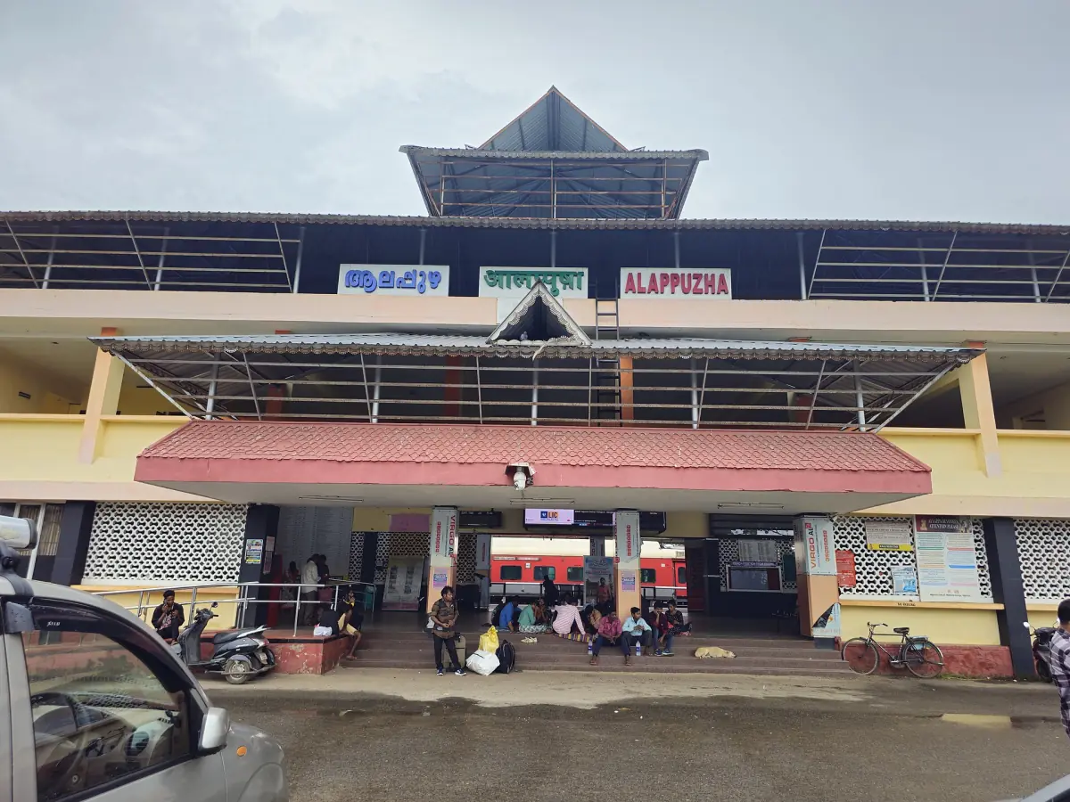 Entrance building of Alappuzha railway station with a tiered roof and parked vehicles