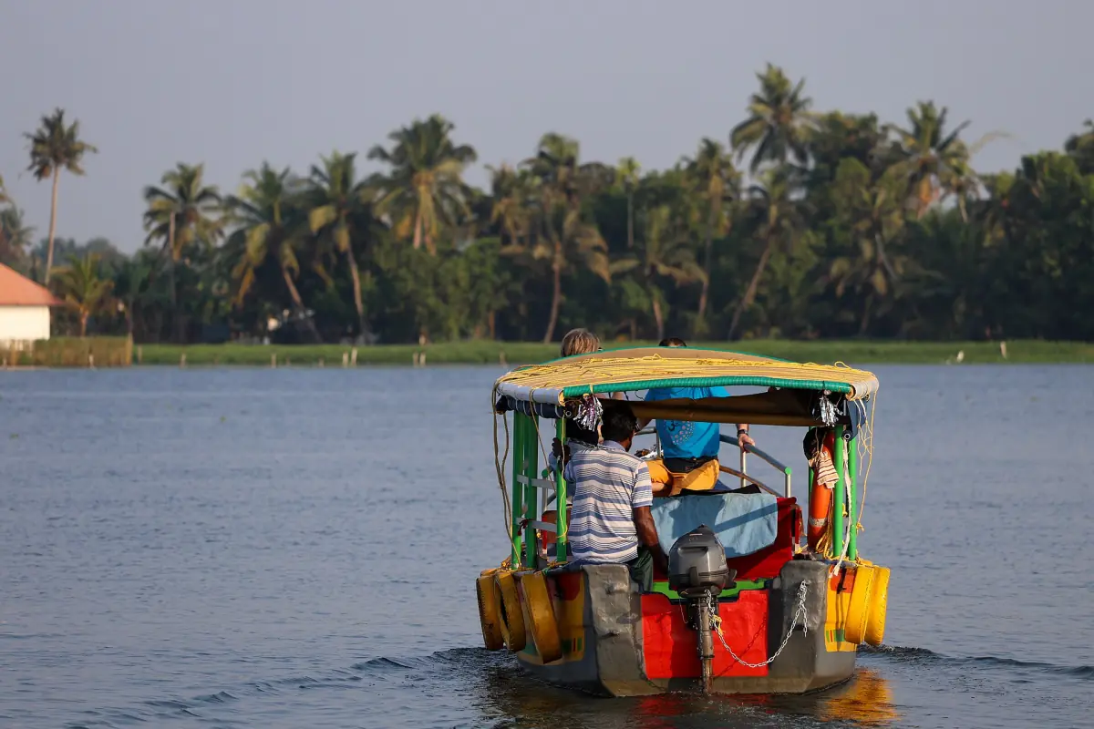 Small canopy motorboat with passengers on a backwater near Alappuzha with palms behind