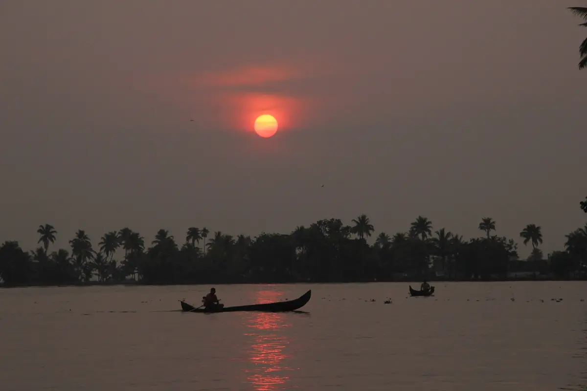 Red sun over palm silhouettes on a Kerala backwater with a small canoe