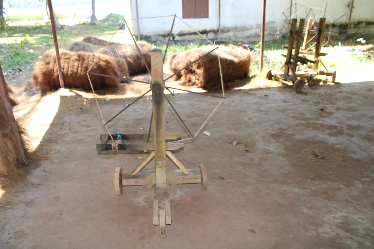 Traditional coir rope spinning wheel with coconut fibre in a sunny yard in Kerala