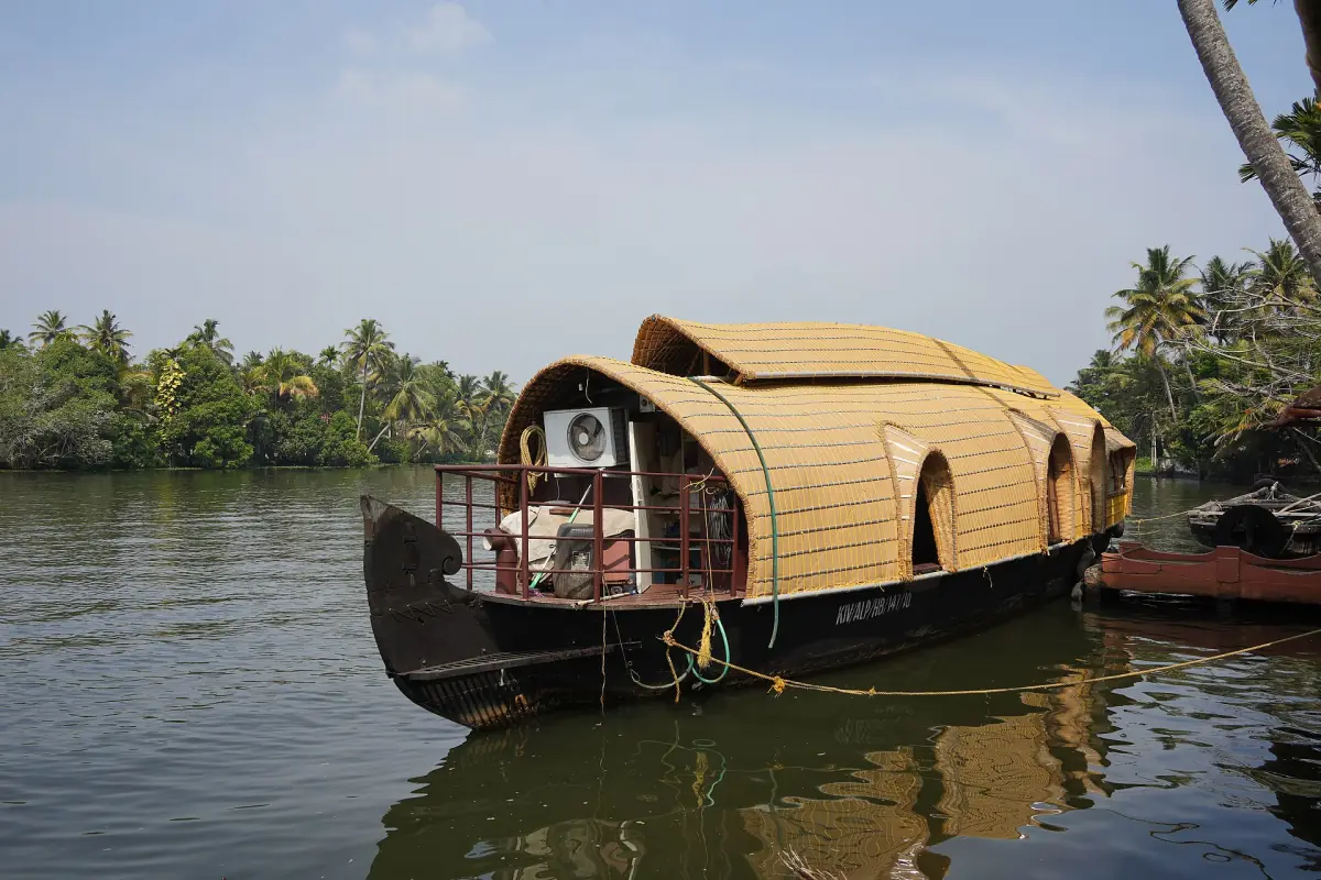 Thatched wooden houseboat with arched roof moored beside trees on a Nedumudy backwater