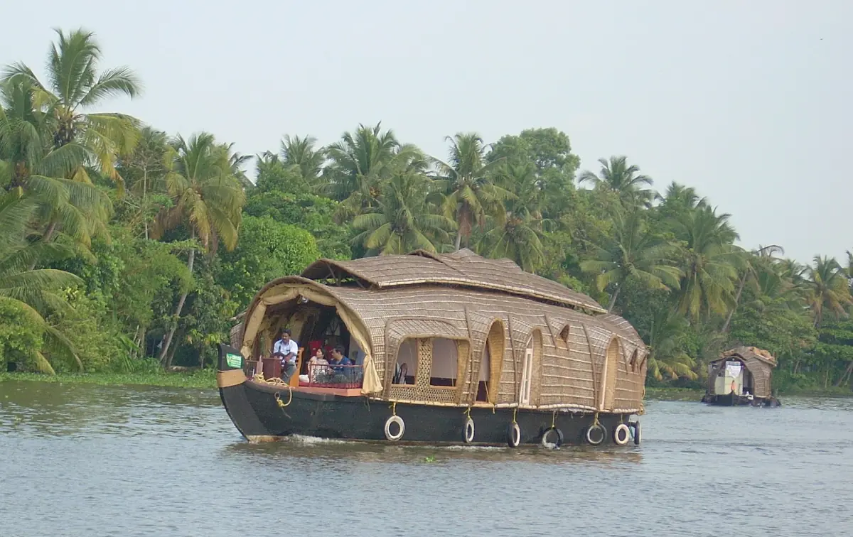Traditional thatched kettuvallam houseboat cruising a palm-lined Kerala backwater in daylight