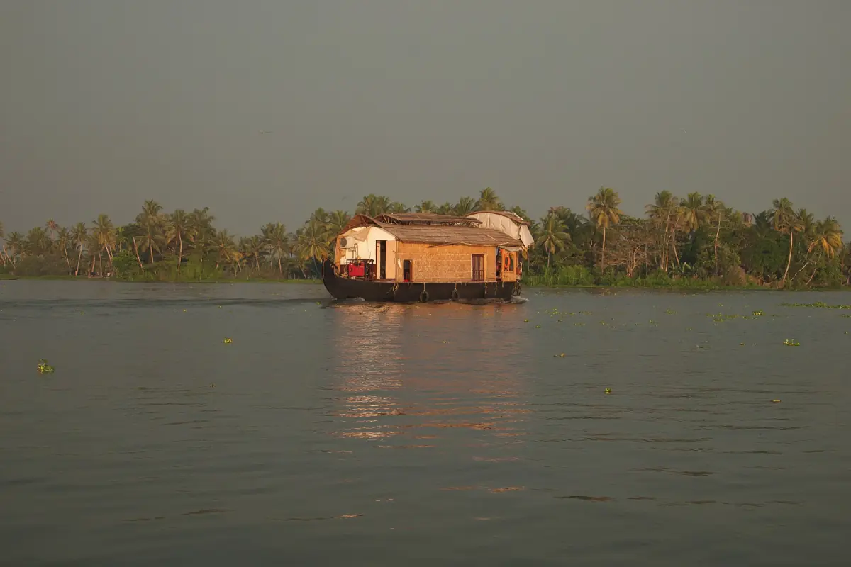 Houseboat on Vembanad Lake in hazy light with a palm-covered island behind