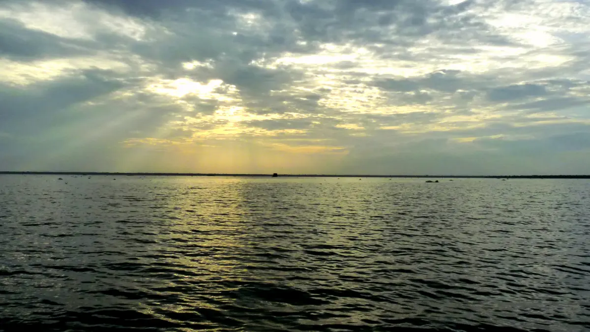 Sunbeams breaking through clouds over the wide calm water of Vembanad Lake